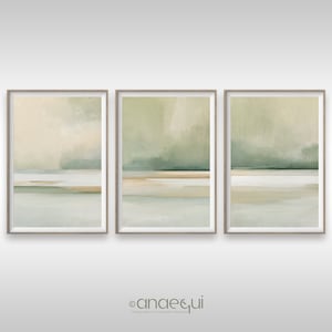 May include: Set of three framed abstract landscape art prints. Each print features a soft color palette of beige, green, and light blue. The artwork has a minimalist style, with horizontal bands of color suggesting a horizon line and sky.