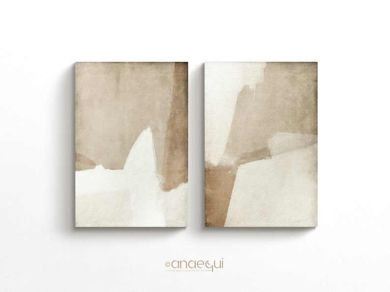 May include: Two abstract art prints. Each print features a beige and white color palette with brushstroke-style shapes. The artwork is displayed on a white background. The prints are rectangular and appear to be canvas.