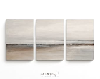 May include: Three-piece abstract canvas art set. Each piece features a minimalist landscape with a neutral color palette of beige, gray, and brown. The artwork depicts a serene beach scene with a horizon line. The canvases are mounted on a white wall.