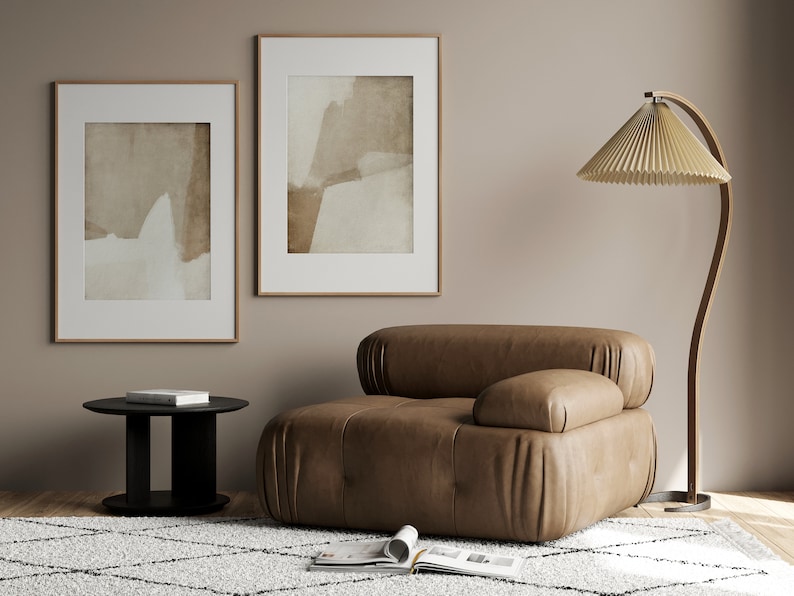 May include: A modern living room scene featuring a brown leather armchair, a black side table, and a floor lamp with a pleated lampshade. Two framed abstract art pieces hang on the wall. A patterned rug and open magazine complete the decor.