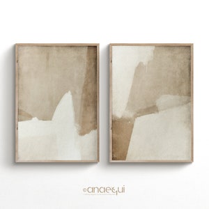 May include: Two framed abstract art prints. Each print features a beige and off-white color palette with overlapping shapes. The artwork is in a wooden frame. The prints are displayed against a white background.