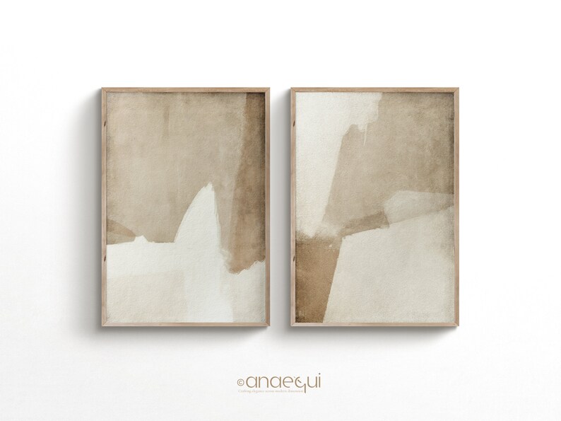 May include: Two framed abstract art prints. Each print features a beige and off-white color palette with overlapping shapes. The artwork is in a wooden frame. The prints are displayed against a white background.