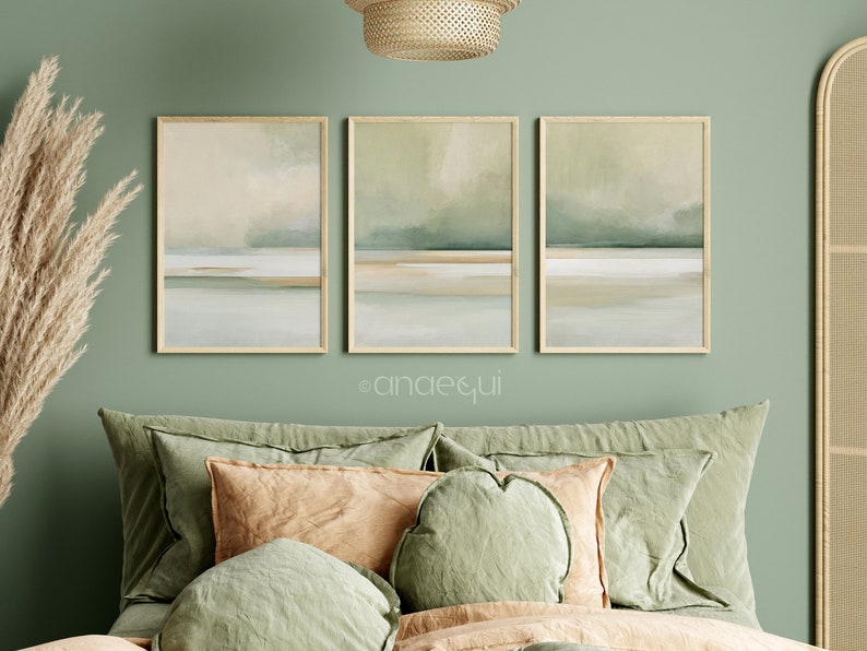 May include: Three framed abstract landscape art prints in muted green, beige, and white tones. The artwork features a minimalist design with horizontal bands of color, evoking a sense of calm. The frames are a light wood color, and the overall aesthetic is modern and serene.