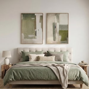 Puede incluir: Una habitación con una cama con cabecero acolchado, ropa de cama verde salvia y cojines decorativos. Dos pinturas abstractas en marcos de madera cuelgan sobre la cama. Una mesita de noche de madera con una lámpara está a la izquierda.