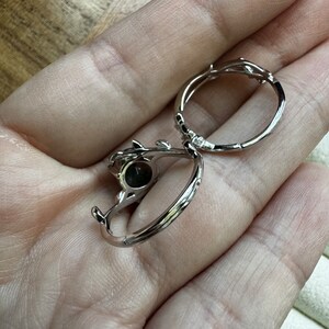 May include: Two silver rings with a delicate, twig-like design. One ring features a dark grey stone.