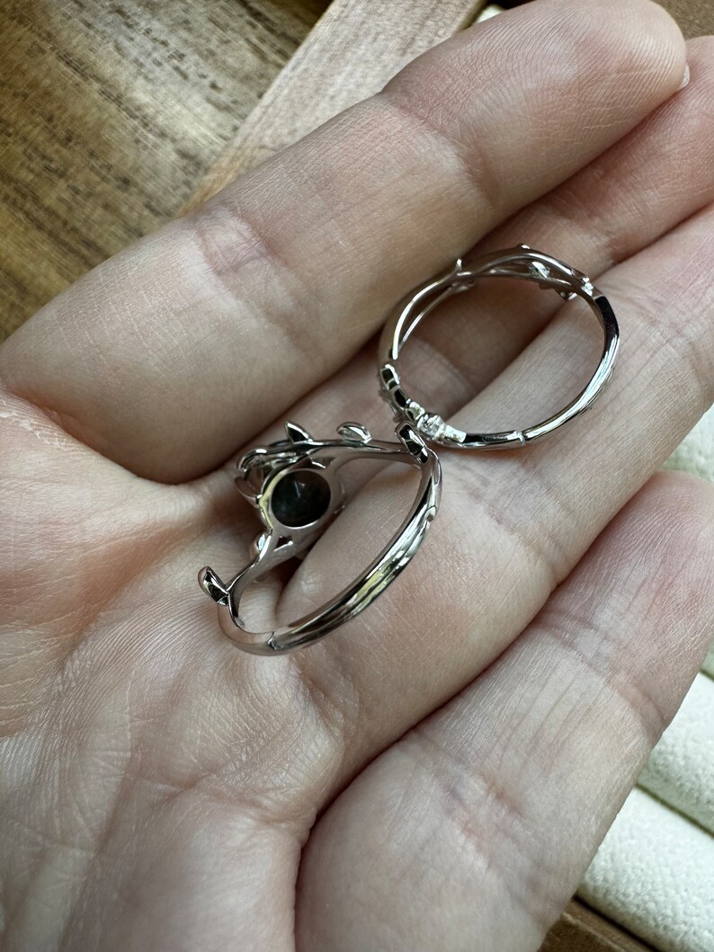 May include: Two silver rings with a delicate, twig-like design. One ring features a dark grey stone.