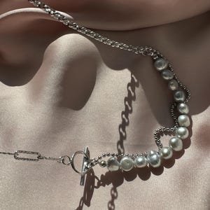 May include: A silver chain necklace with a toggle clasp and a row of off-white pearls.