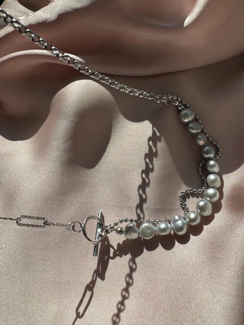 May include: A silver chain necklace with a toggle clasp and a row of off-white pearls.