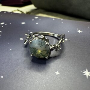 May include: A silver ring with a green and white agate stone set in a leafy design.