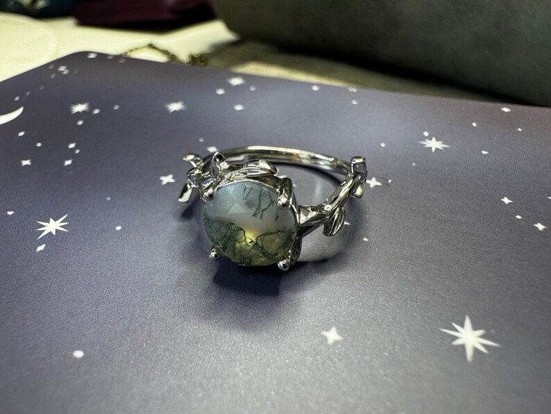 May include: A silver ring with a green and white agate stone set in a leafy design.