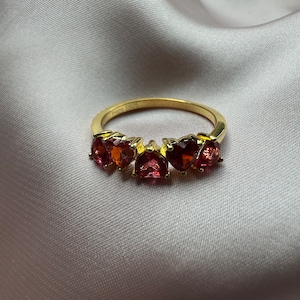 Op de afbeelding: Een gouden ring met vijf rode hartvormige edelstenen.