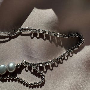 May include: A silver chain necklace with two white pearls. The chain is made of two different styles, one with small round links and the other with larger, more rectangular links.