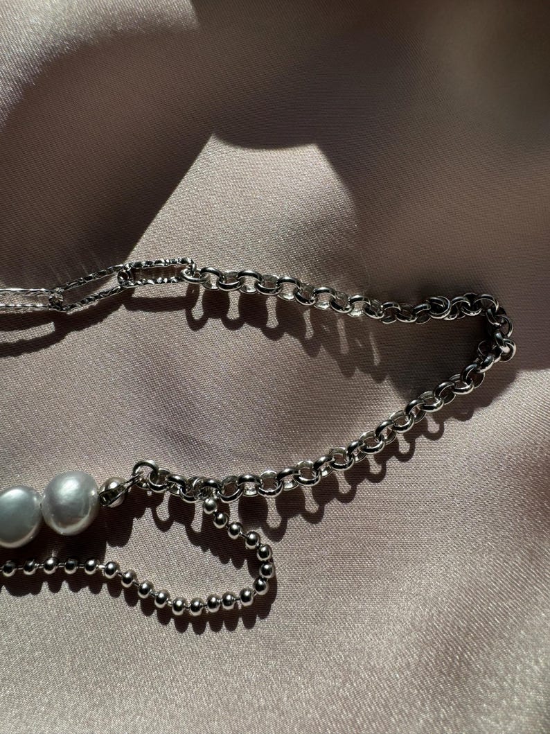 May include: A silver chain necklace with two white pearls. The chain is made of two different styles, one with small round links and the other with larger, more rectangular links.
