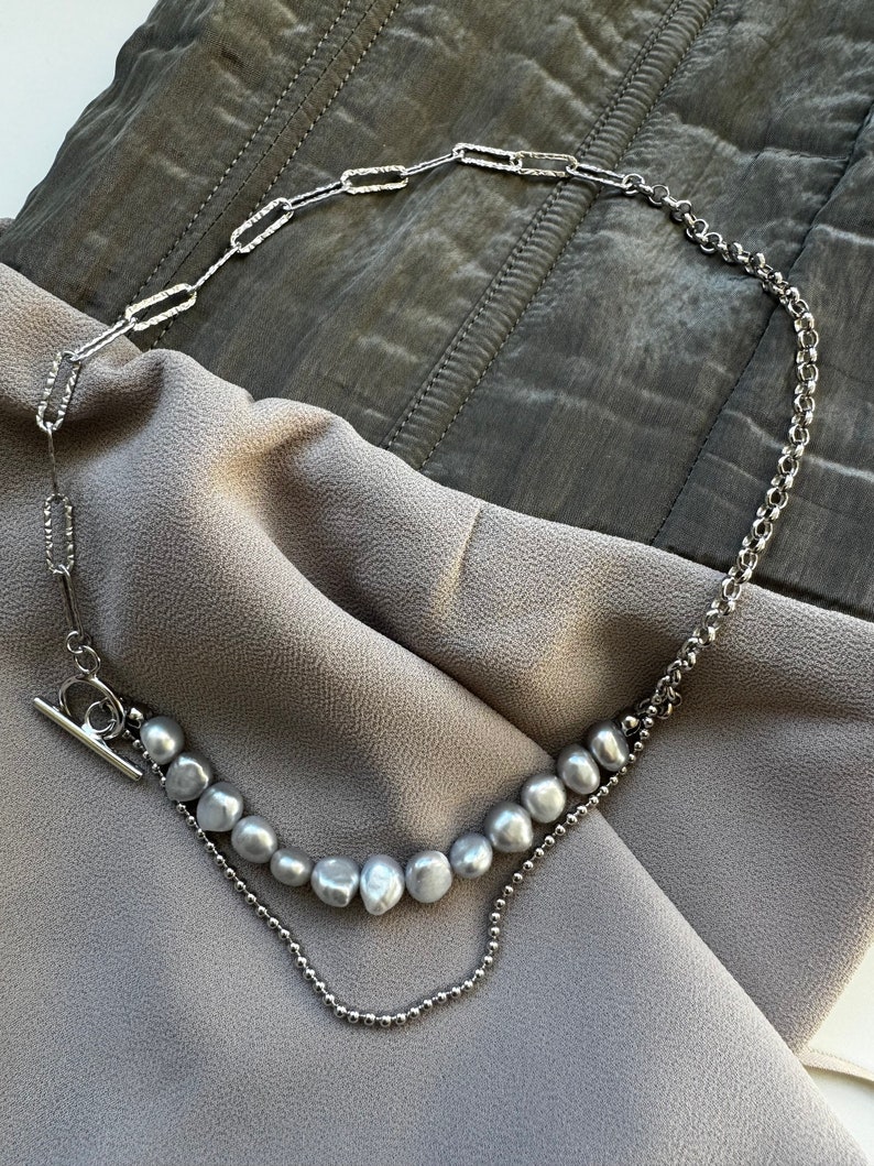 May include: A silver chain necklace with a silver toggle clasp and a strand of gray pearls.