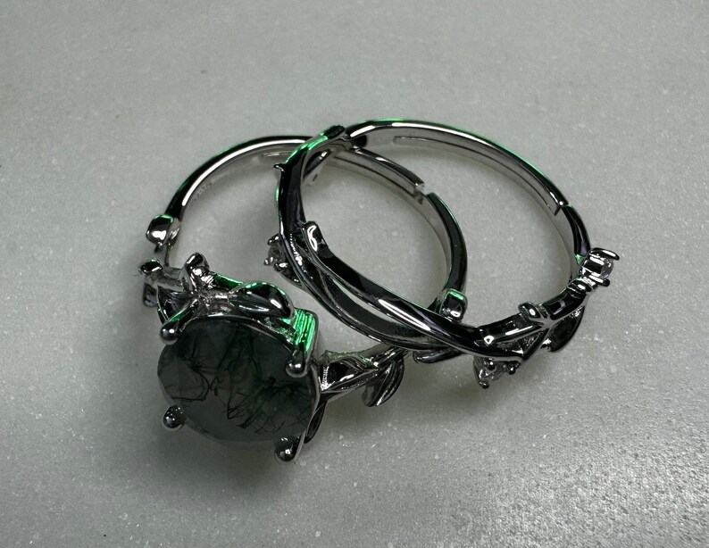 May include: A silver ring set with a large, dark green gemstone. The ring features a delicate, leafy design.