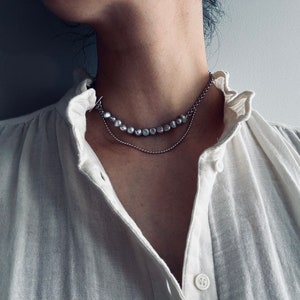 May include: A silver chain necklace with a strand of pearl-like beads. The necklace is layered on top of a thinner silver chain.
