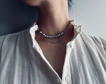 May include: A silver chain necklace with a strand of pearl-like beads. The necklace is layered on top of a thinner silver chain.