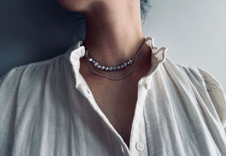 May include: A silver chain necklace with a strand of pearl-like beads. The necklace is layered on top of a thinner silver chain.