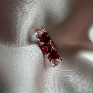 Op de afbeelding: Een zilveren ring met drie hartvormige stenen. De stenen zijn rood en helder.