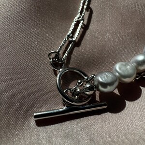 May include: A silver chain necklace with a toggle clasp and a strand of white pearls.