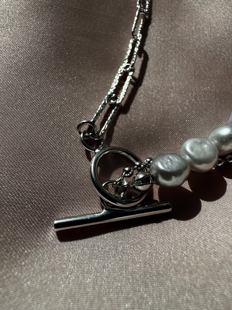 May include: A silver chain necklace with a toggle clasp and a strand of white pearls.