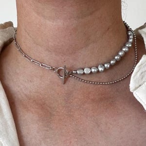 May include: A silver chain necklace with a toggle clasp and a strand of silver-toned pearls.