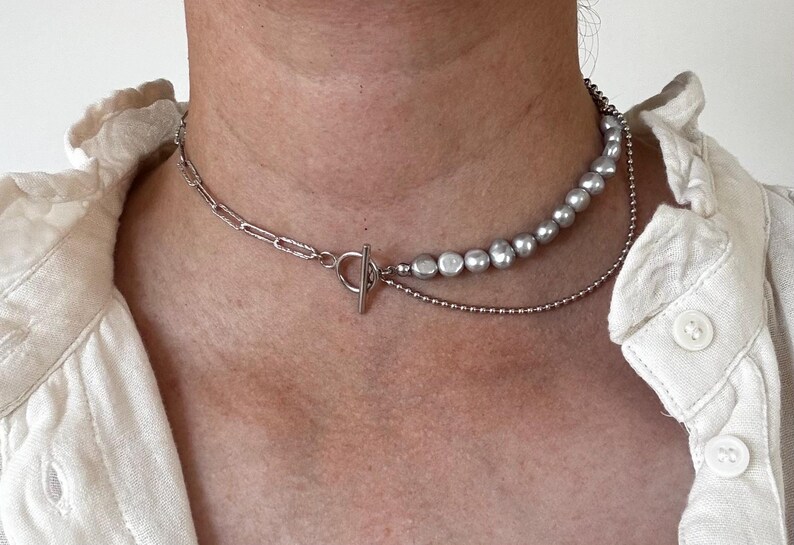 May include: A silver chain necklace with a toggle clasp and a strand of silver-toned pearls.