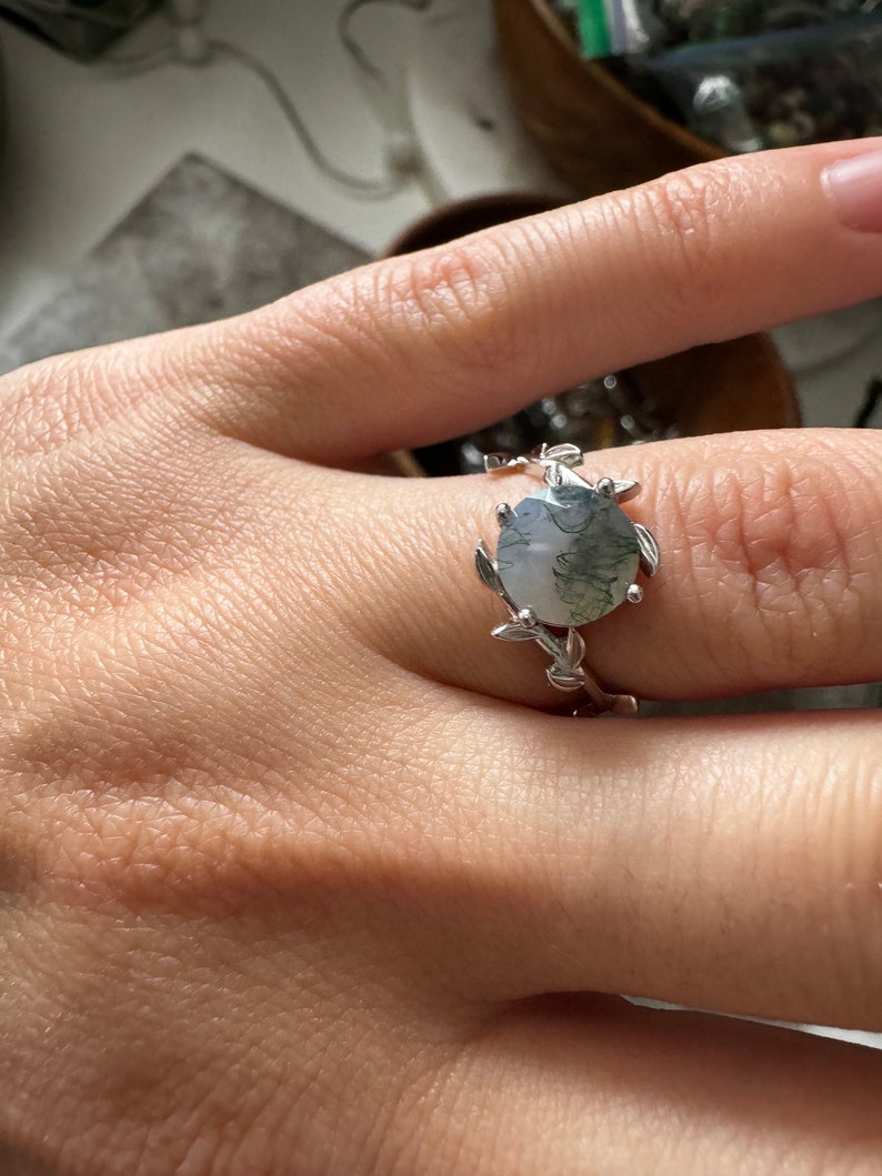 May include: A silver ring with a green and white agate stone set in a leafy design.