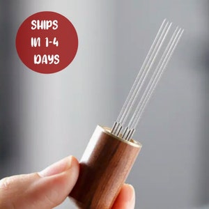 May include: A coffee distributor tool featuring a wooden handle and several thin, stainless steel needles. This tool is designed to evenly distribute coffee grounds in a portafilter before tamping. The image also includes a red circle with the text "SHIPS IN 1-4 DAYS".