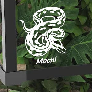 May include: White snake graphic with the name "Mochi" in a cursive font. The snake design is detailed with patterns and curves. The background features green leaves, suggesting a natural or tropical theme.