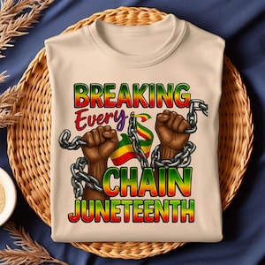 May include: A beige t-shirt with the text "BREAKING EVERY CHAIN JUNETEENTH" in a colourful gradient font. The design shows two clenched fists breaking chains, with a flag in the Pan-African colours.