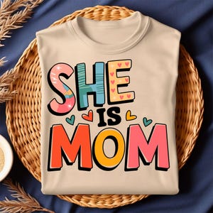 Sie ist Mama - buntes und lustiges Typografie-Design mit Herzen und mutigen Buchstaben, perfekt für Muttertag oder Alltagsfeiern