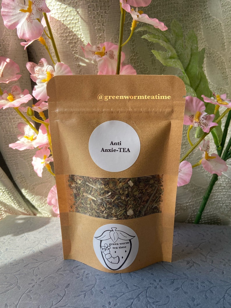 Puede incluir: Una bolsa de papel marr&oacute;n con una etiqueta blanca que dice "Anti Anxie-TEA" y un logotipo de gusano verde. La bolsa contiene t&eacute; de hojas sueltas.