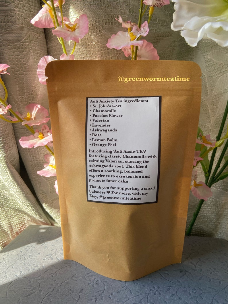 Puede incluir: Una bolsa de papel marr&oacute;n con una etiqueta que dice "Ingredientes del t&eacute; antiansiedad: Hierba de San Juan, manzanilla, flor de la pasi&oacute;n, valeriana, lavanda, ashwagandha, rosa, b&aacute;lsamo de lim&oacute;n, c&aacute;scara de naranja. Presentamos 'Anti Anxie-TEA' con manzanilla cl&aacute;sica y valeriana calmante, protagonizada por la ra&iacute;z de ashwagandha. Esta mezcla ofrece una experiencia relajante y equilibrada para aliviar la tensi&oacute;n y promover la calma interior. Gracias por apoyar un peque&ntilde;o negocio. Para m&aacute;s informaci&oacute;n, visita mi Etsy, @greenwormteatime"