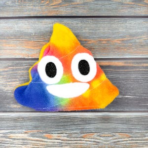 May include: A colorful tie-dye plush toy shaped like a smiling poop emoji. The toy is made of soft, fuzzy fabric and has a rainbow pattern.