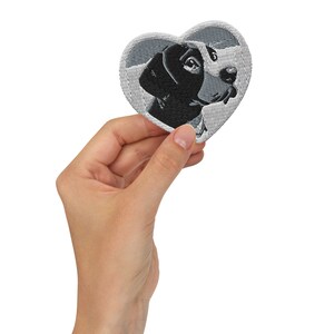 May include: A heart-shaped embroidered patch featuring a black and white dog's head. The patch is gray and has a white outline.