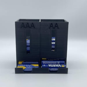 Peut inclure: Un organisateur de piles en plastique noir avec deux compartiments étiquetés "AAA" et "AA". L'organisateur a un tiroir pour chaque compartiment, et les tiroirs sont remplis de piles.