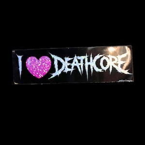 May include: A black sticker with the text "I <3 DEATHCORE" in a white, spiky font. The heart is pink and glittery. The sticker is rectangular and has a holographic sheen.