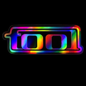 May include: A holographic sticker featuring the word "TOOL" in a rainbow gradient font. The design is set against a black background. The sticker is rectangular with rounded edges, suitable for various applications.