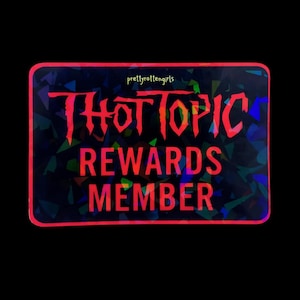 May include: A rectangular sticker with a black background and a red border. The sticker has the words "THOT TOPIC REWARDS MEMBER" in red, stylized lettering. The background has a holographic, geometric pattern. The text "prettyrottengirls" is in the top left corner.