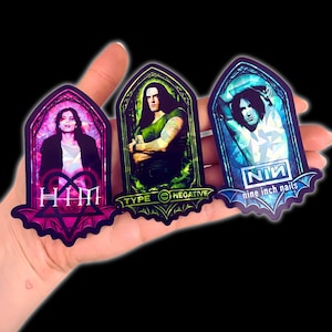 May include: Three stickers featuring band members in a gothic arch design. The stickers include the bands HIM, Type O Negative, and Nine Inch Nails. Each sticker has a unique color scheme and band logo.