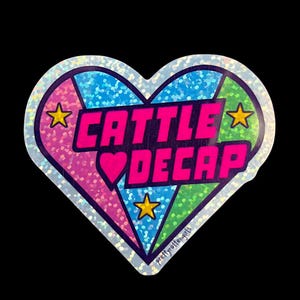 May include: A heart-shaped sticker with a glittery, iridescent border. The sticker is divided into sections of pink, blue, and green. The text "CATTLE DECAP" is in bright pink, with a pink heart and yellow stars.