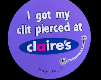 May include: A round, purple button with the text "I got my clit pierced at Claire's" in white. The word "Claire's" is in a blue oval with the "a" in pink. A silver-colored curved barbell is on the right side. The text "prettyrottengirls" is at the bottom.