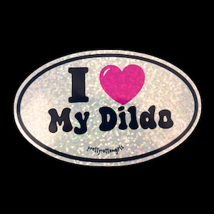 Könnte beinhalten: Ovaler Aufkleber mit glitzerndem silbernen Hintergrund und schwarzem Rand. Der Aufkleber zeigt die Worte "I My Dildo" in Schwarz, mit einem rosa Herz, das das Wort "love" ersetzt. Der Text "prettyrottengirls" ist unten aufgedruckt.