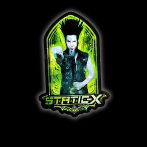 Könnte beinhalten: Ein schwarzer und grüner Static-X-Bandaufkleber mit einem Porträt einer Person mit schwarzen Haaren und einem Spitzbart, die nach vorne zeigt. Das Bandlogo befindet sich unten, mit einem gotischen Rahmen.