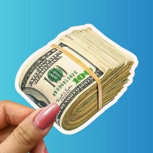 May include: A thick stack of United States one hundred dollar bills secured by a single tan rubber band. The currency features the classic green and cream color palette with visible text including the number 100 and serial number AB 09681382 E.