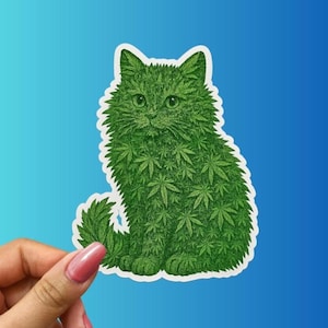 May include: A sticker featuring a green cat illustration. The cat's fur is composed of cannabis leaves. The sticker is held by a hand with pink nail polish against a blue gradient background.