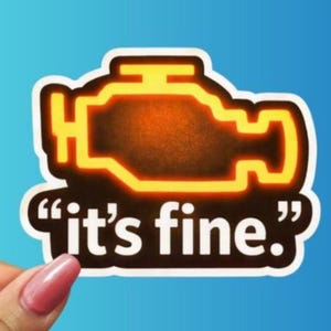 May include: A white sticker with a black outline of a car engine warning light. The engine light is filled with an orange gradient. The text "it's fine." is written in black, inside quotation marks.
