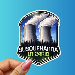 May include: A sticker featuring a stylized illustration of two cooling towers emitting white smoke against a blue sky. The sticker has the text "SUSQUEHANNA U1 24RIO" in a shield-shaped design with a forest silhouette at the bottom.