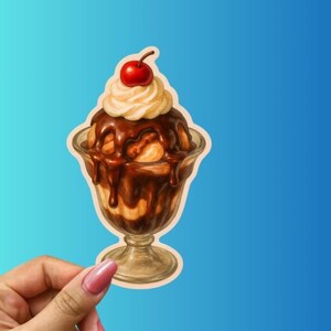 May include: A sticker featuring a detailed illustration of a sundae in a glass. The sundae has vanilla ice cream, chocolate sauce, whipped cream, and a cherry on top. The glass is clear with a stem, and the background is a gradient of blue.